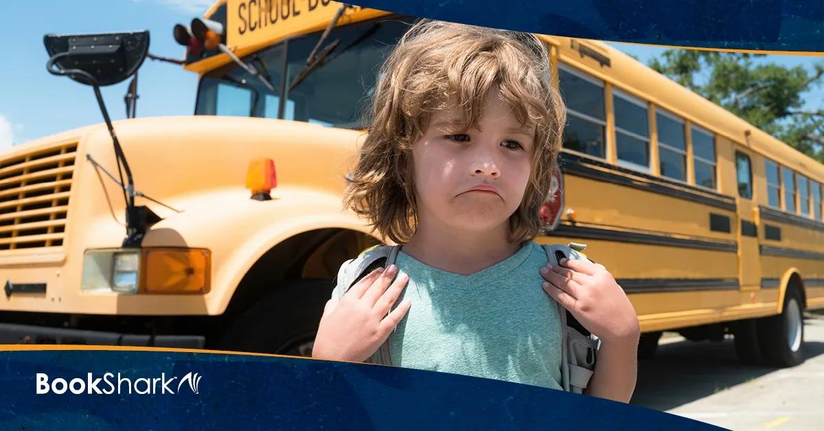 a sad child stands in front of a school bus