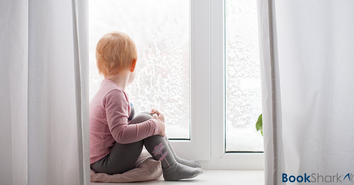 a toddler sits looking out a window to a wintery scene